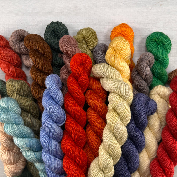 A row of moody, hand-dyed mini skeins arranged on a table, showcasing a cohesive color palette from the Mini Skein Color Story yarn subscription.