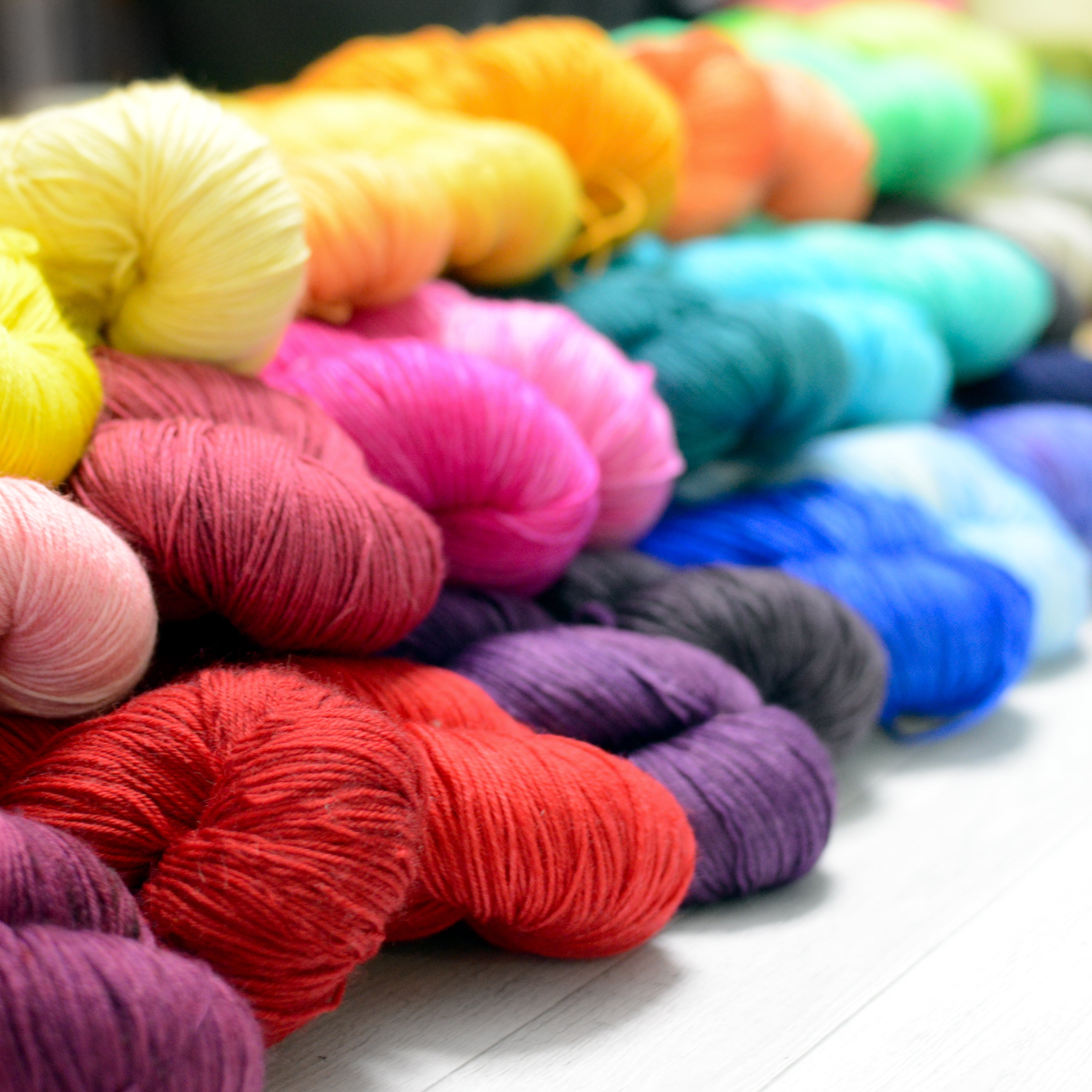 a stack of hand dyed wool yarn in a rainbow of colors red orange yellow green blue purple and neutrals