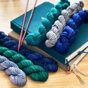 February monthly Color Story Hand Dyed mini skein yarn club subscription from The Woolly Dragon, shown in a pile with an Archer and Olive journal and knitting needles.