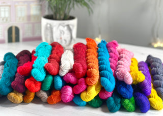 A large pile of hand-dyed mini skeins in a wide range of coordinated colors, showing the variety included in the Mini Skein Color Story yarn subscription.